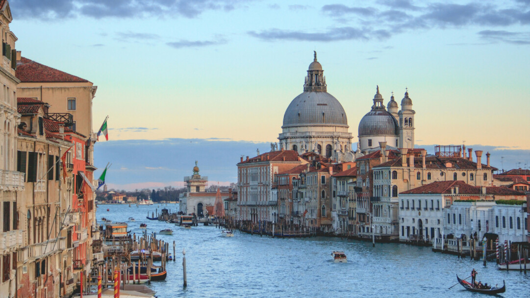 A breathtaking 4K wallpaper captures the enchanting beauty of the Grand Canal at sunset in Venice, Italy. The golden hues of the setting sun cast a warm glow over the tranquil water, illuminating the historic architecture and creating stunning reflections. Ideal for adding a touch of elegance to your desktop or mobile screen.
