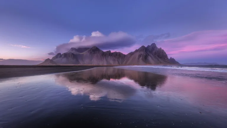A mesmerizing 4K wallpaper capturing the majestic beauty of Vestrahorn Mountain reflected in calm waters. The tranquil scene depicts the towering mountain mirrored perfectly in the serene lake, showcasing the breathtaking landscape of Iceland. Ideal for adorning your desktop or mobile screen with nature's splendor.