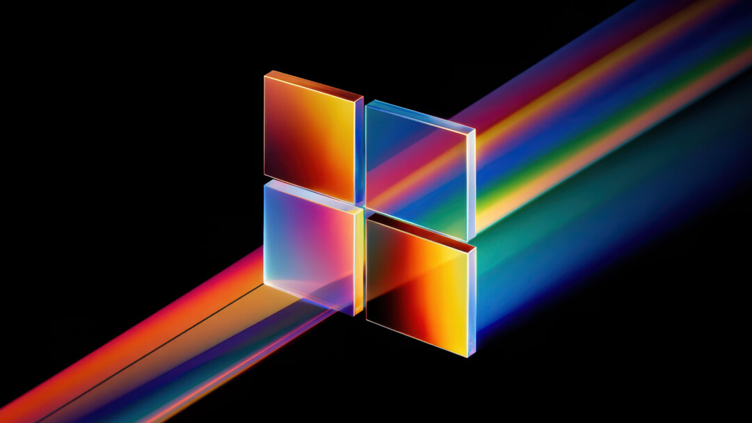 An enchanting 4K wallpaper showcasing the abstract Windows 11 logo, comprised of four translucent, color-shifting squares set against a deep black background. Vibrant prismatic light beams stream diagonally through and behind the logo, creating a dynamic array of warm and cool colors that brilliantly illuminate the scene.