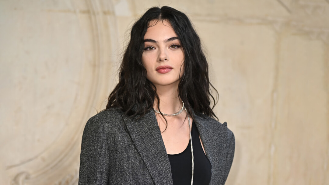 A captivating 4K wallpaper showcases Deva Cassel in a stunning Met Gala portrait, where she stands elegantly composed against a softly blurred, light background. Her direct, calm gaze and flowing dark hair create a sophisticated elegance, highlighted by the subtle texture of her grey blazer and shimmering silver necklace.