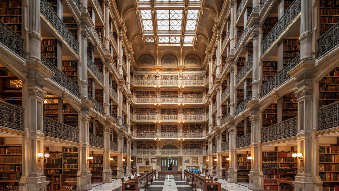 A magnificent 4K wallpaper showcasing Baltimore's George Peabody Library, a grand historic book sanctuary, with its towering five levels of ornate cast-iron balconies and endless shelves of books. Natural light streams from the expansive skylight above, illuminating the warm glow of antique books and intricate gold-leaf details, creating an atmosphere of timeless scholarly elegance.