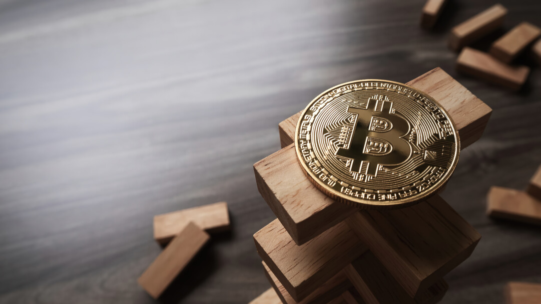 A symbolic 4K wallpaper depicting a gleaming golden Bitcoin digital currency coin delicately balanced atop a Jenga-like tower of wooden blocks on a smooth, dark surface. The coin's brilliant metallic luster sharply contrasts with the matte, textured wood, emphasizing the precarious and transformative nature of cryptocurrency.