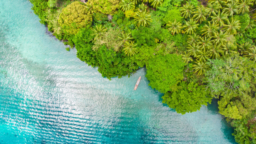 An exquisite 4K wallpaper presents an aerial view of Pulau Ay’s serene blue lagoon and its lush tropical coast. The vibrant turquoise water sparkles under the sun, beautifully contrasting with the dense, verdant island foliage and a solitary boat nestled peacefully near the shore.