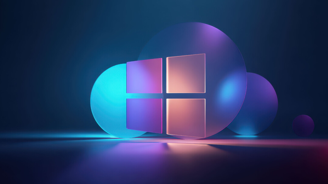 A radiant 4K wallpaper featuring a sleek, modern Windows logo composed of four translucent square panes, set against a deep blue, minimalist background with glowing circular forms. Vibrant gradients of neon blue, purple, and orange light illuminate the translucent materials, creating a luminous, futuristic art piece with soft reflections on the dark surface below.