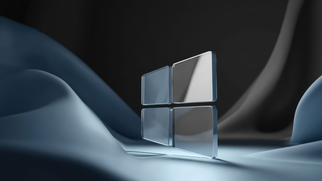 A stunning 4K wallpaper showcases a translucent glass 3D Windows logo, subtly illuminated against a backdrop of flowing, dark blue and grey abstract curves. The polished surfaces of the logo and its environment reflect light, creating a serene interplay of highlights and shadows that emphasize the image's clean, futuristic aesthetic.