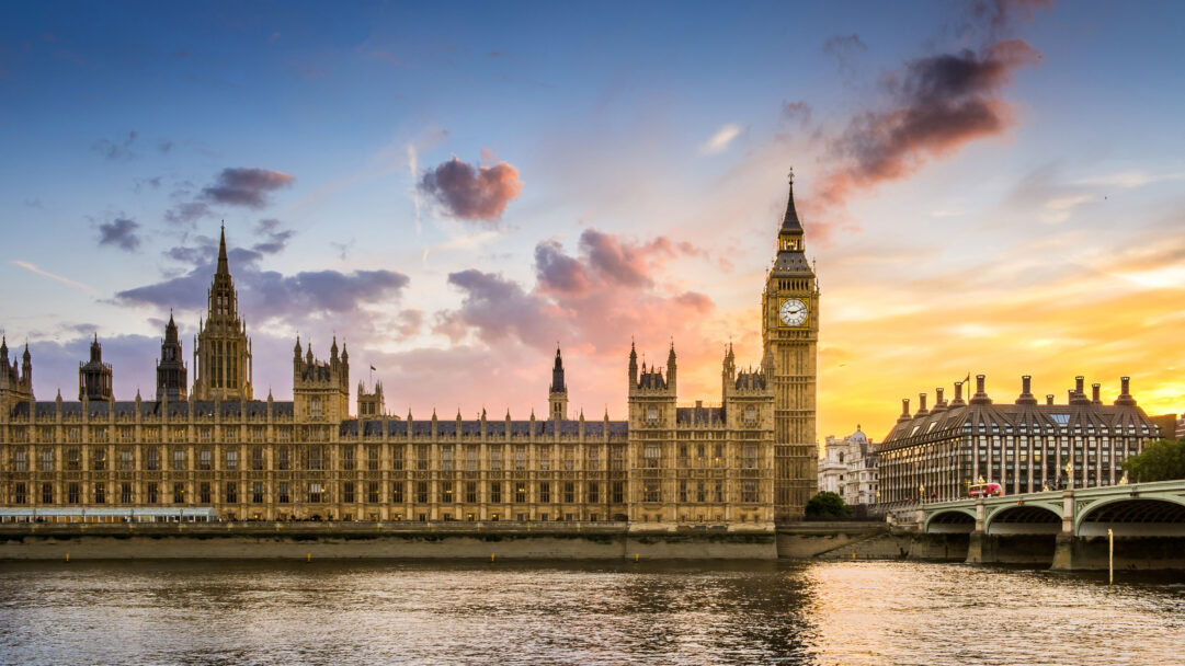 An iconic 4K wallpaper presents the Houses of Parliament and Big Ben standing grandly by the River Thames during a stunning London sunset. The vibrant sky transitions from deep blue to fiery orange and soft pinks, casting a magical glow over the historic architecture and tranquil water.