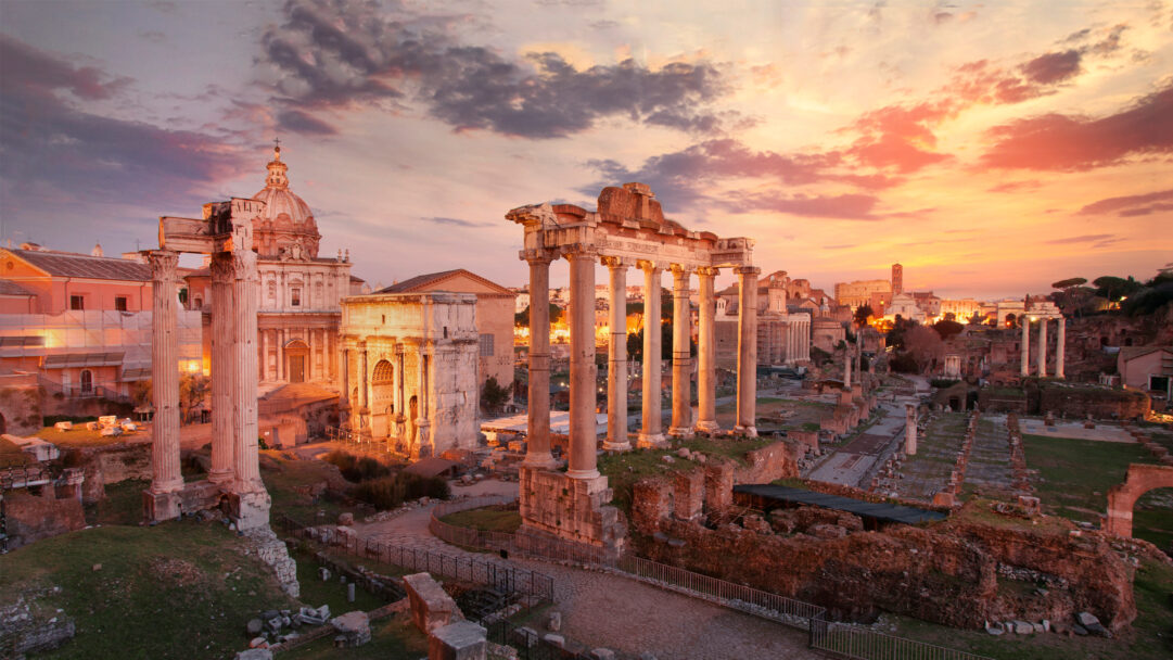 A breathtaking 4K wallpaper showcasing the ancient Roman Forum, with the grand columns of the Temple of Saturn rising majestically amidst other historical ruins. The sky is ablaze with a stunning sunset, painting the clouds in vibrant shades of orange, pink, and purple, beautifully illuminating the weathered stone and evoking a sense of enduring history.