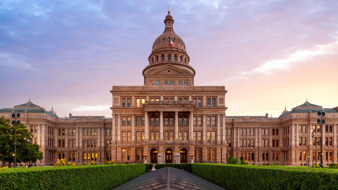 A grand 4K wallpaper captures the Texas State Capitol in Austin, majestically centered amidst its manicured grounds at dusk. The building's warm stone facade glows against a dramatic sunset sky, transitioning from soft lavender to golden hues, creating a serene and timeless atmosphere.