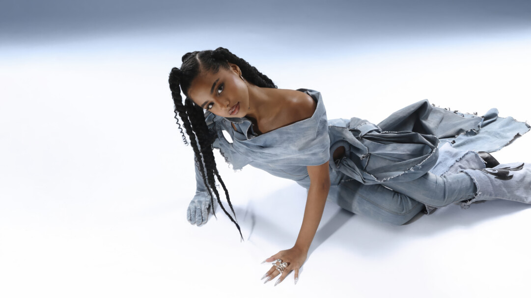 An exquisite 4K wallpaper presenting Tyla, the iconic celebrity, in a striking pose against a minimalist gradient studio background. Her unique deconstructed denim ensemble, bold silver rings, and elaborate braided hairstyles perfectly encapsulate her distinctive and powerful fashion sense.