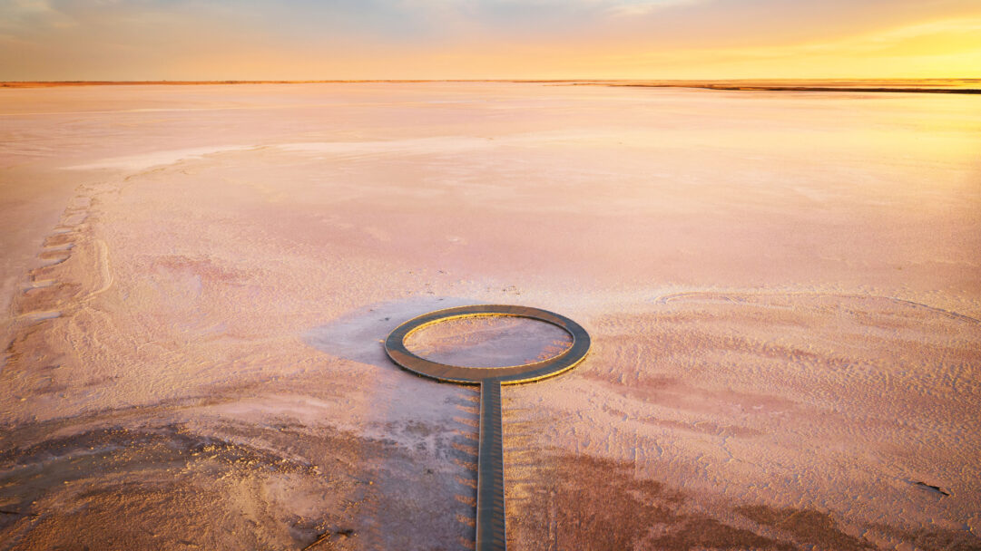A magical 4K wallpaper of Lake Tyrrell, Victoria, Australia, depicts a vast, reflective pink salt lake under a sunset sky, with a modern boardwalk extending into its expanse. The interplay of golden light and pastel pink hues creates an ethereal landscape, culminating in the striking circular viewing platform at the boardwalk's end.