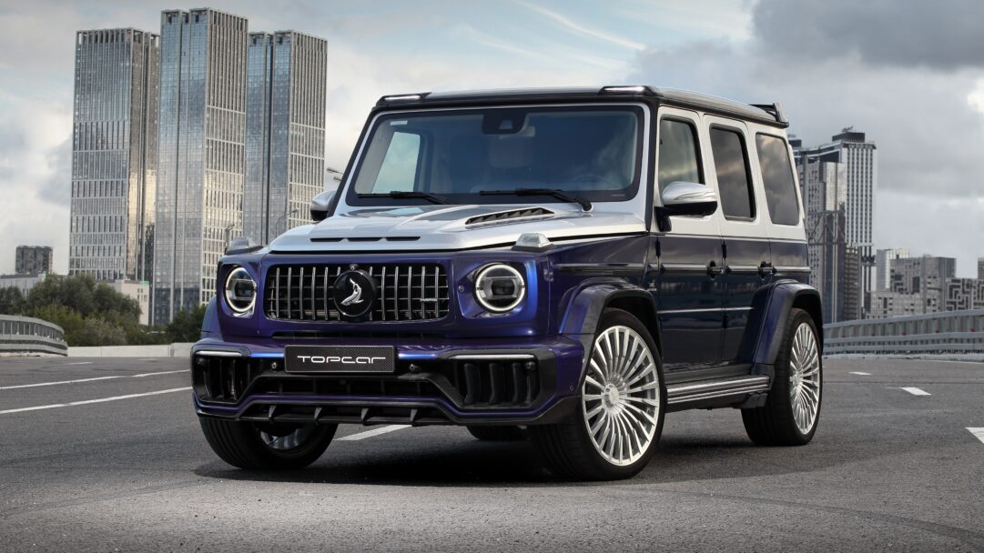 A commanding 4K wallpaper featuring a custom two-tone Mercedes-Benz G-Class TopCar Design SUV, parked prominently on an urban road. Its striking metallic dark blue and silver finish, complemented by the aggressive TopCar body kit and large polished wheels, exudes luxury against the backdrop of towering modern city skyscrapers.
