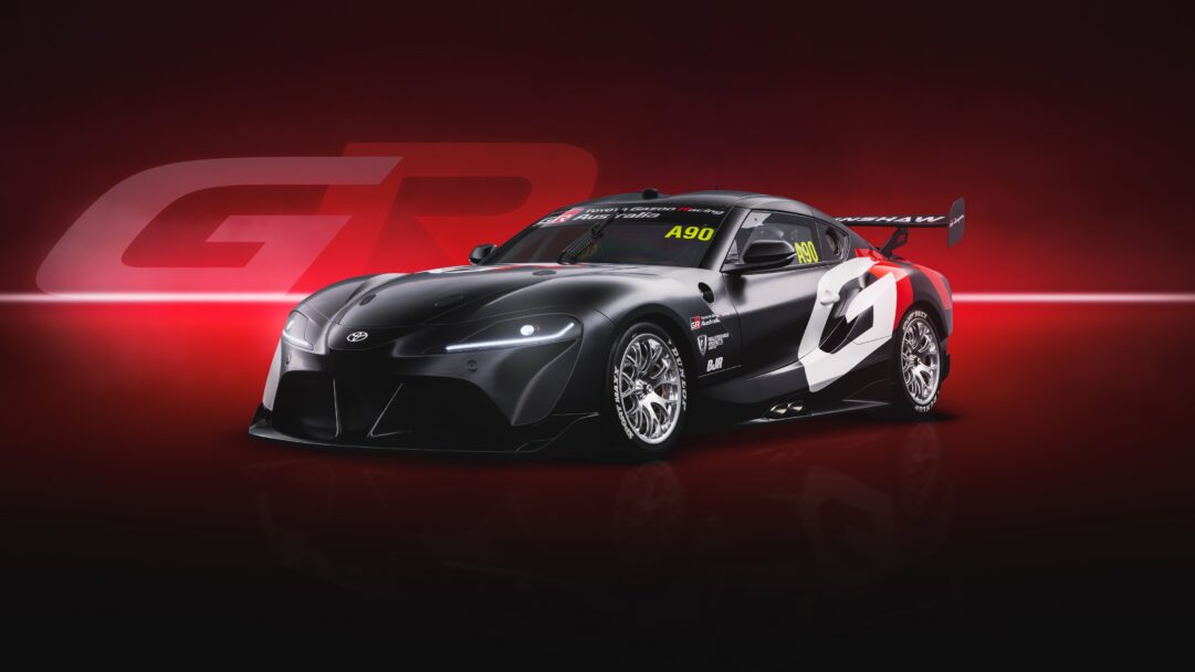 A dynamic 4K wallpaper presents a sleek, matte black Toyota GR Supra Racing Supercar, adorned with white and red racing decals, parked on a reflective surface against a rich, gradient red background. Its piercing LED headlights and metallic wheels shimmer, contrasting with the car's matte finish and the deep red hues of the backdrop, creating an intense, high-performance atmosphere.