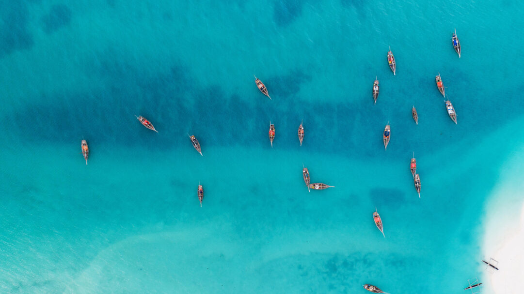 A breathtaking 4K wallpaper showcasing numerous traditional wooden fishing boats scattered across the strikingly turquoise waters off Kendwa Beach in Zanzibar. The remarkable clarity of the vibrant blue water reveals the shallow sandy seabed, perfectly defining the tranquil, idyllic tropical mood.