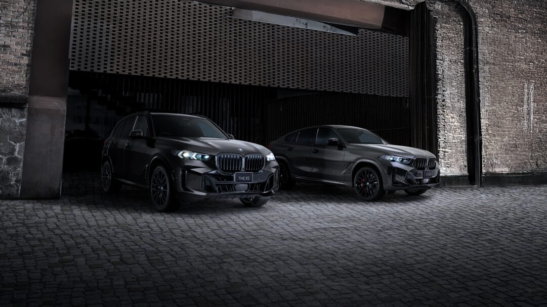 An exclusive 4K wallpaper showcases the sleek BMW X5 Edition Shadow and BMW X6 Edition Shadow, parked side-by-side on dark cobblestones in a moody, industrial-style setting. Their deep, almost black finishes and minimal chrome accents are dramatically lit, highlighting their powerful silhouettes against the dim, textured brick and metallic backdrop, perfectly capturing their 'Shadow' edition essence.