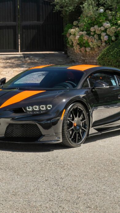 A dynamic 4K wallpaper showcasing a Bugatti Chiron Super Sport 300+ in black with bold orange racing stripes, parked on a sunlit asphalt driveway in front of a grand black gate framed by vibrant green foliage. The car's glossy finish reflects the bright daylight, emphasizing its powerful lines and the vivid contrast of the orange accents against the deep black body.