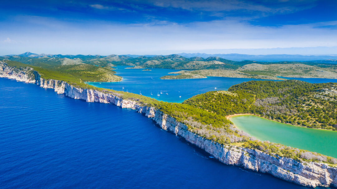 A magnificent 4K wallpaper showcases the dramatic white Cliffs of Tela Ica Nature Park, soaring above the deep blue sea with a backdrop of numerous forested islands and distant hills under a clear sky. The vivid contrast between the sheer rock faces, the lush green vegetation atop them, and the serene turquoise lake nestled behind creates a captivating sense of untouched natural beauty.