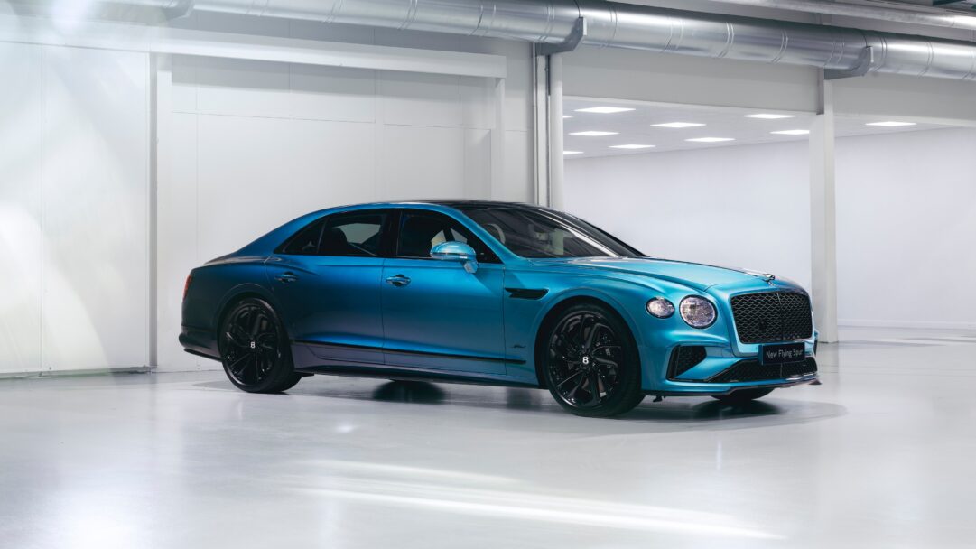 An exquisite 4K wallpaper showcasing the Mulliner Bentley Flying Spur Speed, a luxurious blue sedan, perfectly poised in a minimalist, brightly lit studio. Its vibrant metallic blue paint, contrasted by glossy black accents and wheels, gleams under the soft studio lights, conveying elegance and powerful sophistication.