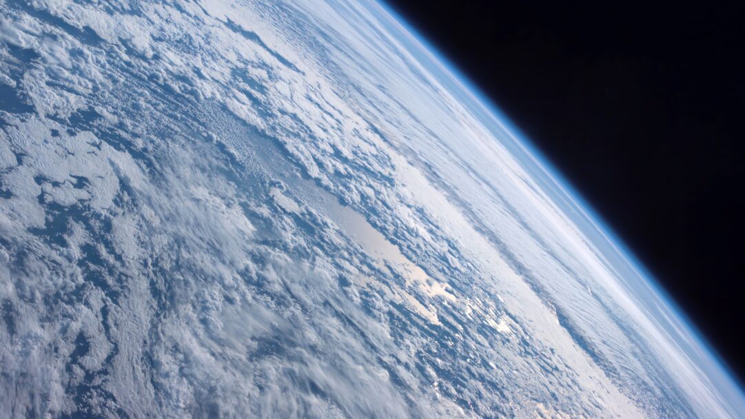 A mesmerizing 4K wallpaper captures the iconic OS X Mountain Lion space view of Planet Earth, featuring a dynamic tapestry of white clouds swirling across the deep blue of our world. The brilliant Sun glinting off ocean waters through breaks in the clouds, contrasted with the delicate atmospheric glow against the profound blackness of space, evokes a sense of wonder and vastness.