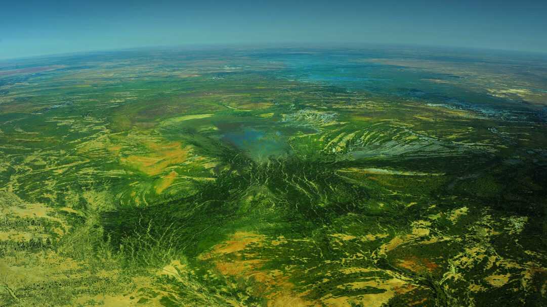 A mesmerizing 4K wallpaper offers an expansive aerial view of the Channel Country in Outback Queensland, Australia, revealing a vast landscape of interconnected watercourses and diverse terrain. Intricate patterns of vibrant green vegetation, ochre earth, and shimmering blue water form a dramatic, organic tapestry under a clear blue horizon.