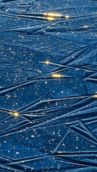 A dazzling 4K wallpaper showcasing the patterned blue ice of Alam-Pedja Nature Reserve in Estonia. Golden sunlight sprinkles across the deep blue surface, creating a magical, starry sparkle.