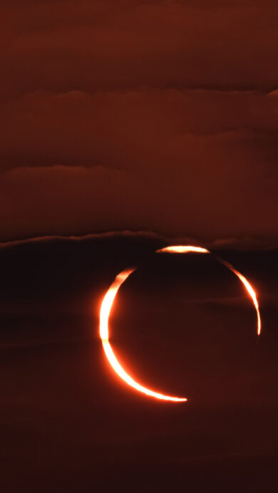 A spectacular 4K wallpaper captures an annular solar eclipse, forming a brilliant 'Ring of Fire' visible against the dark, cloudy sky over Doha, Qatar. The intense, fiery orange ring of the sun glows brightly through parting clouds, casting a dramatic, mystical reddish hue across the darkened celestial expanse.