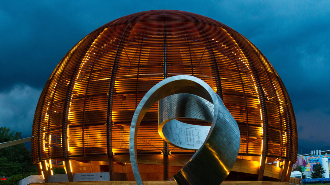 A mesmerizing 4K wallpaper showcases the architectural grandeur of the Globe of Science and Innovation Building at night, glowing with warm light against a dramatic dark blue sky. Its intricate wooden shell radiates a vibrant orange, beautifully juxtaposed with the sleek, curving silver sculpture etched with scientific formulas, enhancing the mood of innovation and wonder.