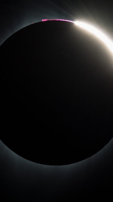 An awe-inspiring 4K wallpaper capturing the dramatic 'Diamond Ring' effect of the 2017 Total Solar Eclipse as seen from Madras, Oregon. The moon perfectly obscures the sun, revealing a single dazzling point of sunlight and a thin arc of vibrant pink solar prominences against the deep black sky.