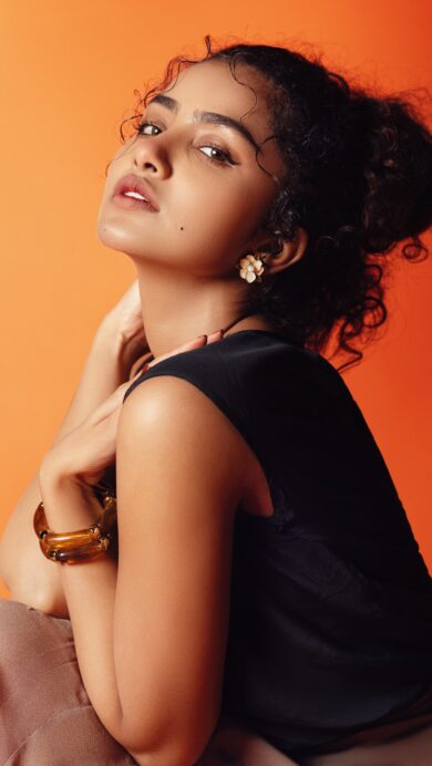 A radiant 4K wallpaper displays Anupama Parameswaran in a captivating photoshoot, posing confidently against a striking orange-red gradient background. Her elegant pose and direct gaze are beautifully illuminated by the warm, transitioning colors, creating a vibrant and sophisticated mood.