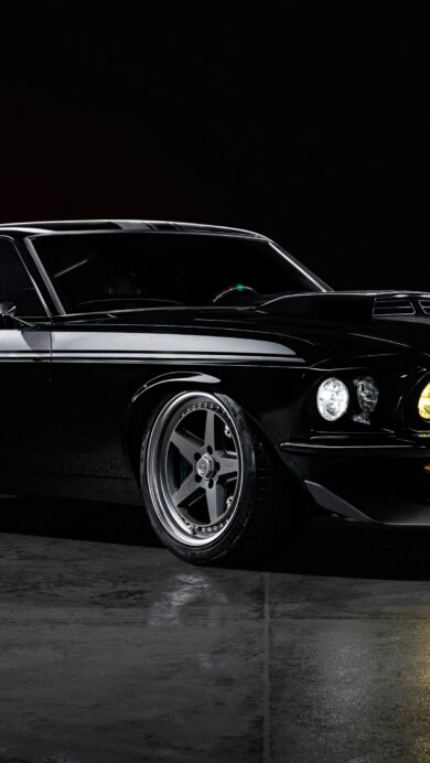 An iconic 4K wallpaper showcasing a black classic Ford Mustang muscle car, parked on a gleaming wet dark floor against a subtly lit dark background. Its sleek, glossy body reflects the ambient light, while the glowing yellow headlights pierce through the darkness, emphasizing its potent and mysterious presence.