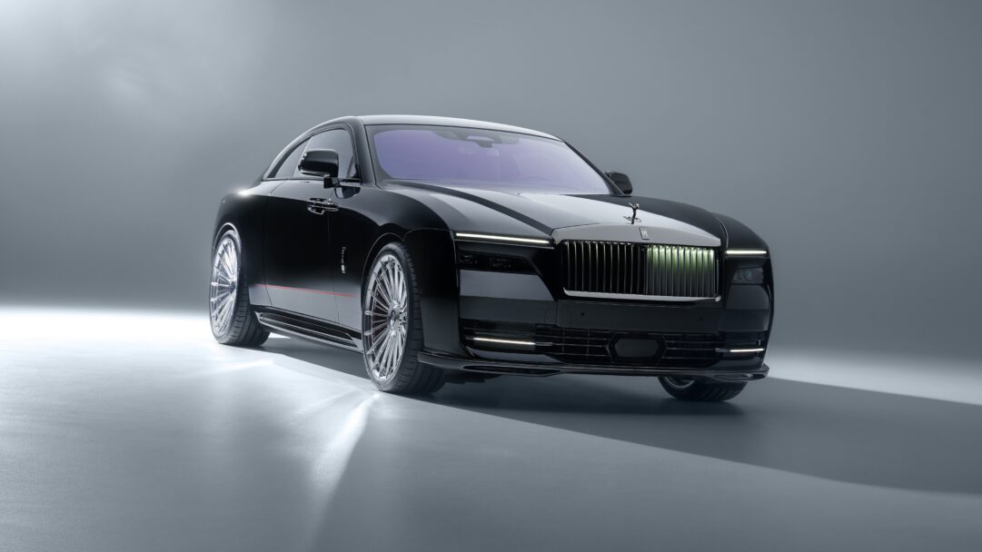 An exquisite 4K wallpaper presenting a sleek black Rolls-Royce Spectre EV luxury car, positioned angled in a minimalist, light grey studio setting. Its glossy black body reflects the pristine lighting, highlighting the illuminated grille, bright headlights, and intricate chrome wheels that emphasize its modern opulence.