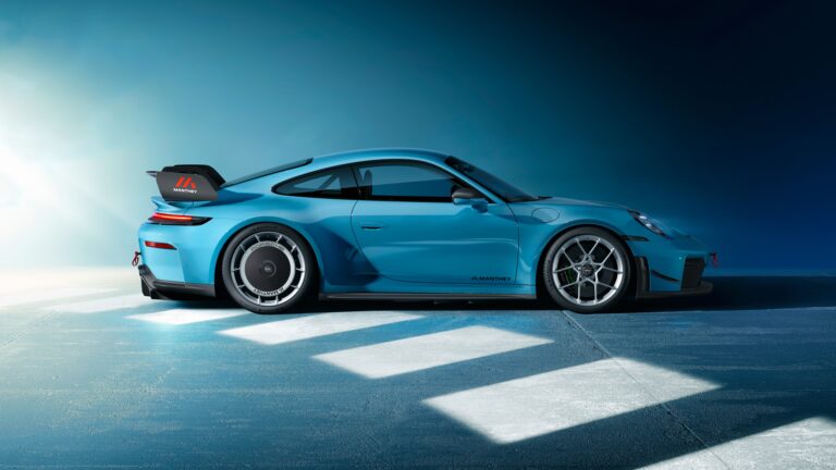 A captivating 4K wallpaper presenting a vibrant blue Porsche 911 GT3 Manthey sports car parked in profile on a textured blue-grey floor against a gradient blue background. Sharp geometric light reflections illuminate the ground beneath the car, highlighting its sleek design and the subtle Manthey branding on its carbon fiber rear wing and wheels, creating a cool, modern aesthetic.