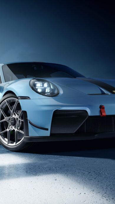 A mesmerizing 4K wallpaper showcasing a brilliant blue Porsche 911 GT3 sports car parked on a textured concrete floor in a dimly lit studio. Intense light from the left illuminates its sleek profile and glowing headlights, creating a dynamic contrast against the dark background.
