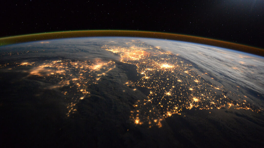 An awe-inspiring 4K wallpaper capturing Earth at night from the International Space Station, revealing vast networks of city lights across continents. These brilliant golden clusters dramatically illuminate the darkened landmasses, creating a mesmerizing interplay of human presence against the deep cosmic expanse and the glowing atmospheric edge.