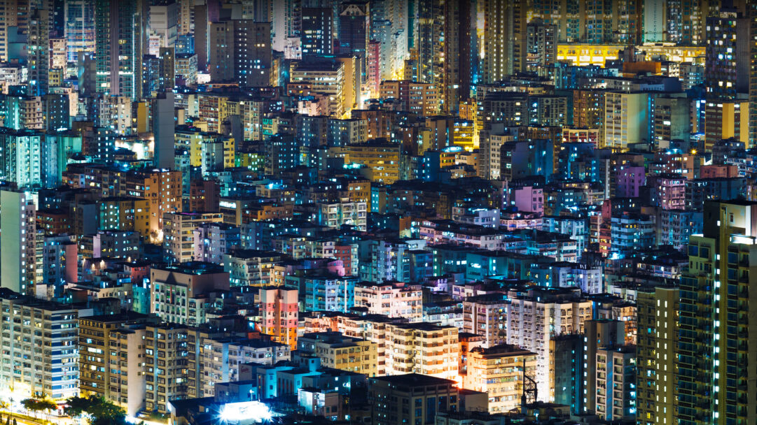 A vibrant 4K wallpaper showcasing the iconic night city buildings of Hong Kong SAR, stretching endlessly across the frame. Thousands of windows illuminate the dense architecture with a captivating interplay of warm amber and cool blue lights, creating a bustling urban tapestry.