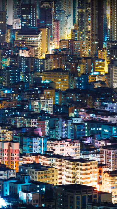 A vibrant 4K wallpaper showcasing the iconic night city buildings of Hong Kong SAR, stretching endlessly across the frame. Thousands of windows illuminate the dense architecture with a captivating interplay of warm amber and cool blue lights, creating a bustling urban tapestry.