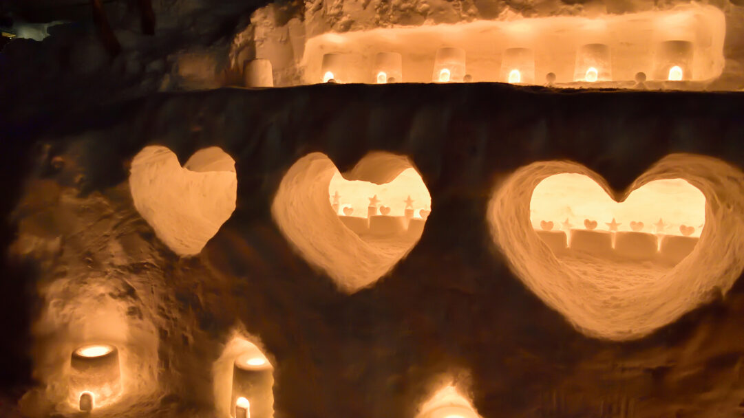 A magical 4K wallpaper of illuminated heart carvings and snow sculptures at the Otaru Snow Light Path Festival in Hokkaido, Japan. Warm golden light spills from the heart-shaped openings, illuminating delicate star and heart carvings within and casting an enchanting glow on the surrounding snow.
