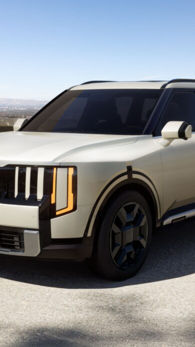 A pristine 4K wallpaper featuring a light beige Kia Telluride SUV parked on a modern concrete driveway. The bright sunlight creates sharp shadows, highlighting the vehicle's contemporary design against a backdrop of distant hills and a clear blue sky.