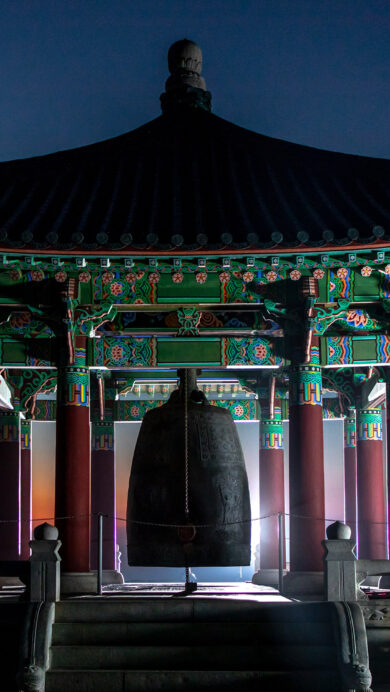A captivating 4K wallpaper presents the Korean Bell of Friendship pavilion in Los Angeles at sunset. Its ornate green and red traditional Korean architecture is dramatically silhouetted against a vibrant gradient of orange and deep blue twilight sky.