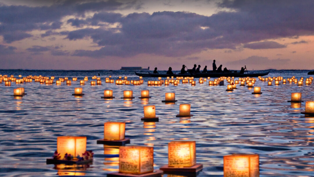 A captivating 4K wallpaper capturing the serene Lantern Floating Ceremony at Ala Moana Beach Park in Honolulu, Hawaii, as countless illuminated lanterns drift across the water. The warm, golden light of the floating lanterns casts a mesmerizing glow on the dark, rippling ocean, contrasting beautifully with the deep purples and blues of the twilight sky.