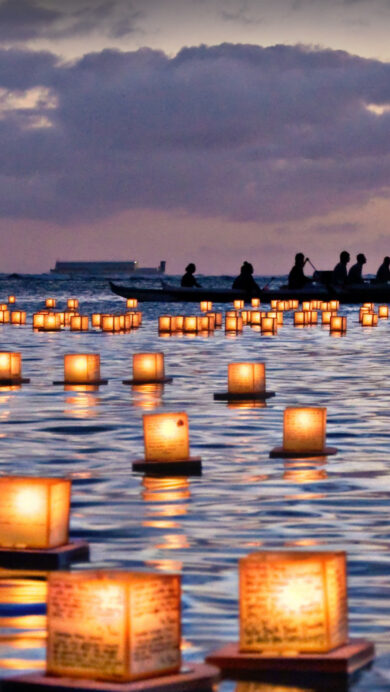 A captivating 4K wallpaper capturing the serene Lantern Floating Ceremony at Ala Moana Beach Park in Honolulu, Hawaii, as countless illuminated lanterns drift across the water. The warm, golden light of the floating lanterns casts a mesmerizing glow on the dark, rippling ocean, contrasting beautifully with the deep purples and blues of the twilight sky.