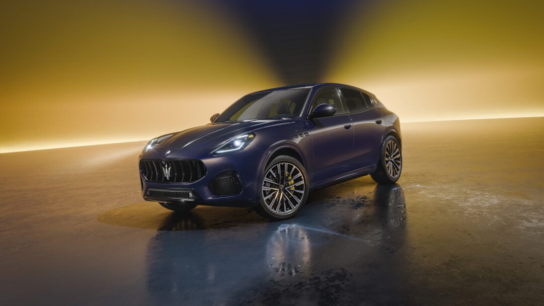 A captivating 4K wallpaper showcasing a dark blue Maserati Grecale SUV, angled slightly right, parked in a dimly lit studio against a striking golden backdrop. Dynamic golden light streams from behind, reflecting off the car's sleek body and creating a dramatic, wet-look sheen on the dark, reflective floor, emphasizing its powerful and luxurious presence.