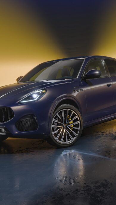 A captivating 4K wallpaper showcasing a dark blue Maserati Grecale SUV, angled slightly right, parked in a dimly lit studio against a striking golden backdrop. Dynamic golden light streams from behind, reflecting off the car's sleek body and creating a dramatic, wet-look sheen on the dark, reflective floor, emphasizing its powerful and luxurious presence.
