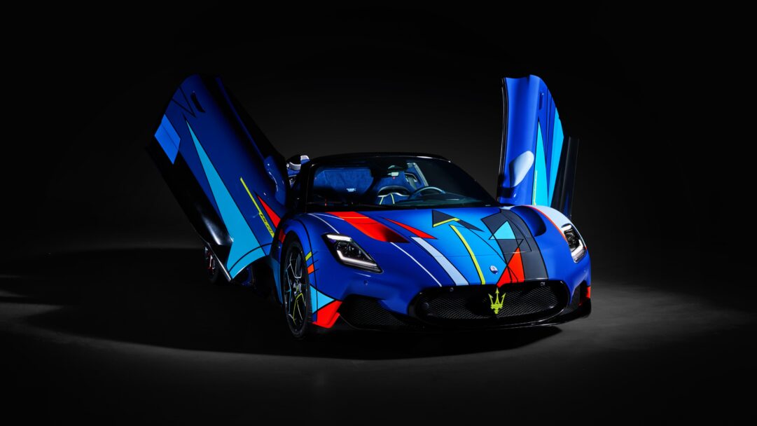 An electrifying 4K wallpaper showcasing a Maserati MC20 supercar with an abstract blue design, prominently displayed with its butterfly doors open against a dark, minimalist setting. The car's vibrant abstract livery of blue, red, yellow, and white geometric shapes creates a powerful, artistic statement, further enhanced by the dramatic lighting that emphasizes its sleek, aggressive contours.
