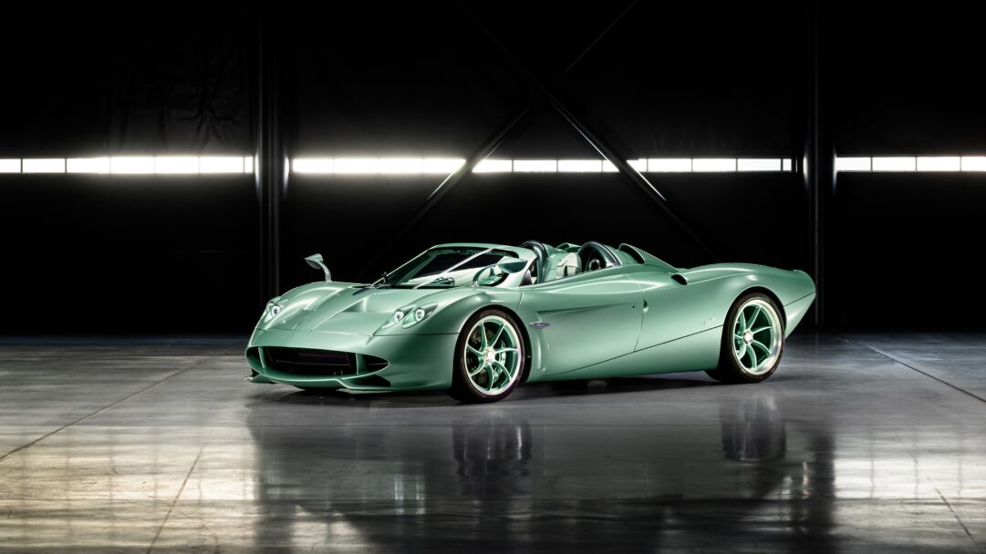 An exquisite 4K wallpaper presenting a pristine mint green Pagani Huayra Roadster centered in a dimly lit professional studio. Its metallic mint green finish gleams under precise studio lighting, reflecting onto the polished dark floor and emphasizing its aerodynamic lines against the stark black backdrop.