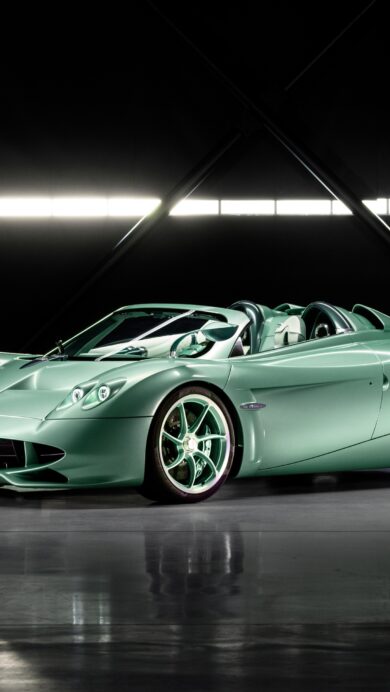 An exquisite 4K wallpaper presenting a pristine mint green Pagani Huayra Roadster centered in a dimly lit professional studio. Its metallic mint green finish gleams under precise studio lighting, reflecting onto the polished dark floor and emphasizing its aerodynamic lines against the stark black backdrop.
