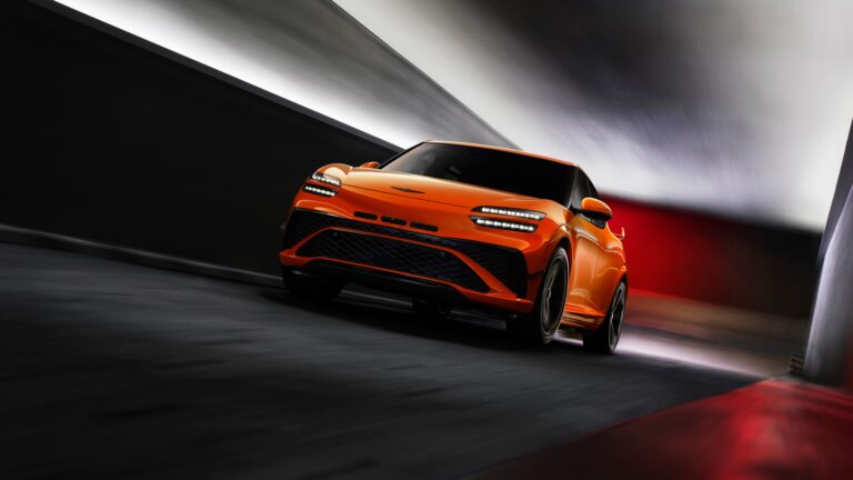 An exhilarating 4K wallpaper featuring an orange car speeding through a dark, modern tunnel. Its vibrant orange body, highlighted by piercing LED headlights, contrasts sharply with the blurred concrete walls, creating a powerful sense of velocity and futuristic elegance.