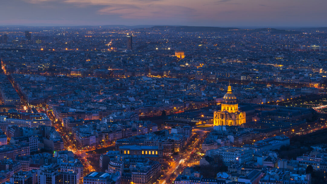 An enchanting 4K wallpaper of a sprawling Paris night cityscape, prominently featuring the illuminated Les Invalides dome and the distant Arc de Triomphe. Golden streetlights and landmark illuminations warmly contrast against the deep blue twilight, creating a vast, glittering expanse that defines the city's vibrant nocturnal mood.