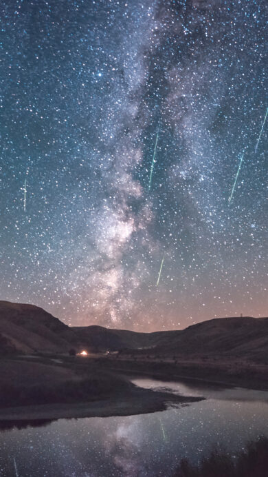 A celestial 4K wallpaper depicting the Perseid Meteor Shower and the majestic Milky Way arching over Cottonwood Canyon State Park in Oregon. Numerous bright meteors streak across the dark night sky, their glowing trails and the Milky Way's band reflecting in the winding river below, creating a profound sense of cosmic wonder.