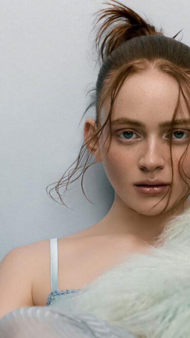 A captivating 4K wallpaper showcasing Sadie Sink, with her wet hair pulled into a high ponytail and wet strands framing her face, gazing directly at the viewer while partially obscured by soft green fur against a pale blue background. The glistening wet hair and the ethereal texture of the pastel green fur create a striking interplay of dampness and softness, defining an intense yet serene mood.