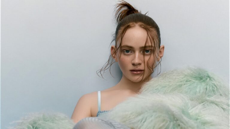 A captivating 4K wallpaper showcasing Sadie Sink, with her wet hair pulled into a high ponytail and wet strands framing her face, gazing directly at the viewer while partially obscured by soft green fur against a pale blue background. The glistening wet hair and the ethereal texture of the pastel green fur create a striking interplay of dampness and softness, defining an intense yet serene mood.